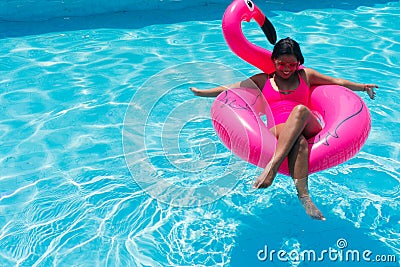 Woman in bikini relaxes on inflatable pink flamingo in swimming pool. Attractive woman in swimsuit lies in the sun Stock Photo