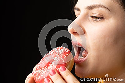 A woman bites a large red donut, a black background, a place for text. Gluttony, overeating and sugar addict. Stock Photo