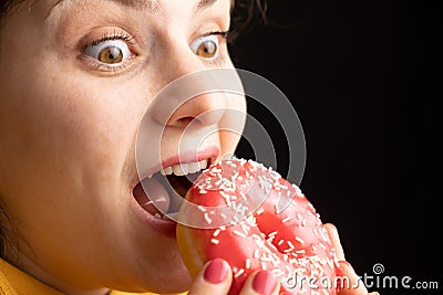 A woman bites a large red donut, a black background, a place for text. Gluttony, overeating and sugar addict. Stock Photo