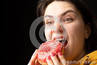 A woman bites a large red donut, a black background, a place for text. Gluttony, overeating and sugar addict. Stock Photo