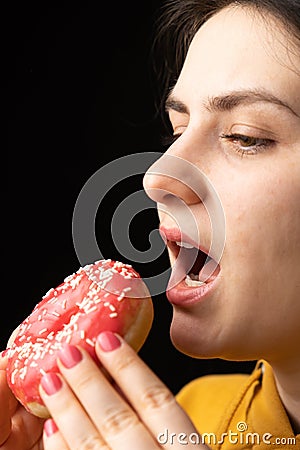 A woman bites a large red donut, a black background, a place for text. Gluttony, overeating and sugar addict. Stock Photo