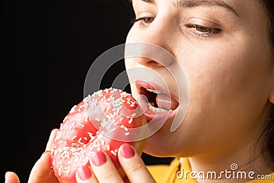 A woman bites a large red donut, a black background, a place for text. Gluttony, overeating and sugar addict. Stock Photo