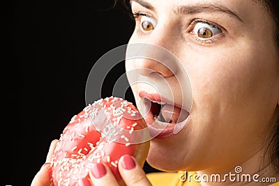 A woman bites a large red donut, a black background, a place for text. Gluttony, overeating and sugar addict. Stock Photo