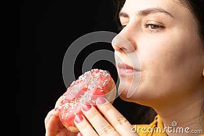 A woman bites a large red donut, a black background, a place for text. Gluttony, overeating and sugar addict. Stock Photo