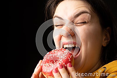 A woman bites a large red donut, a black background, a place for text. Gluttony, overeating and sugar addict. Stock Photo