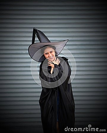 Woman with black cape and witch hat use her hands to strangle her neck on stripe metal background Stock Photo