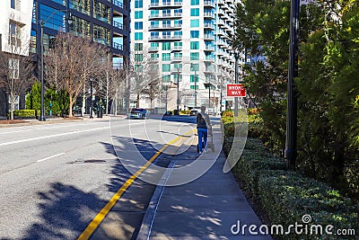 A woman in a black jacket and jeans pushing a stroller along the sidewalk surrounded by buildings, bare winter trees Editorial Stock Photo