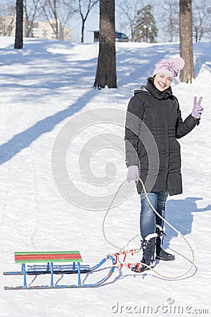 A woman in a black winter jacket with sledges in a snow-covered park or forest. vertical photo Stock Photo