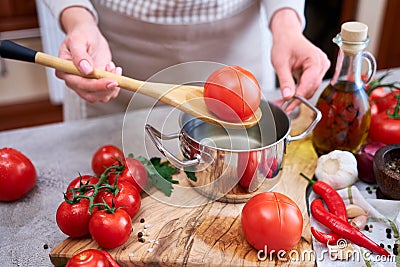 woman blanching a tomato holding over pan with hot water for further peeling Stock Photo