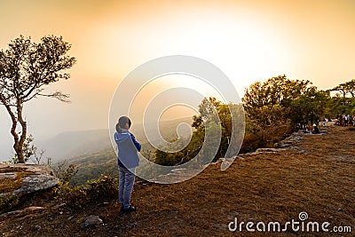 Woman in blue coat looking sunset at cliff in winter Stock Photo