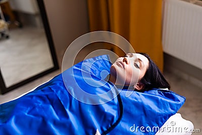 Woman in blue pressotherapy suit lying down having pressure therapy for weight loss in spa salon. Doctor help lose weight and Stock Photo