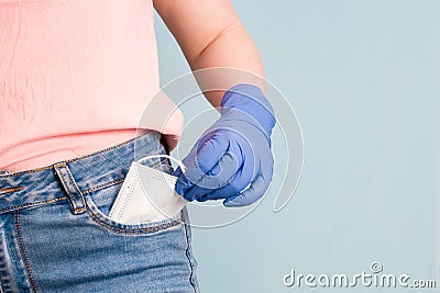 a woman in blue rubber gloves puts a protective face mask in her front jeans pocket, blue background, copy space Stock Photo