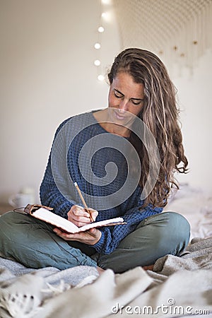 Woman in blue sweater writing in journal Stock Photo