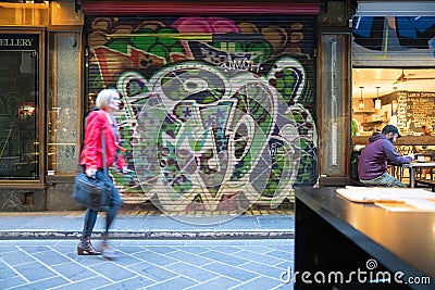 Woman blurred in motion walking past closed roller door of business Editorial Stock Photo