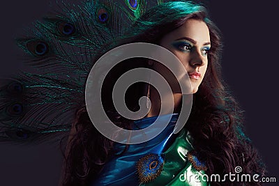 Woman in brilliant blue dress with peacock feathers design. Creative fantasy makeup, long dark hair fluttering at wind. Stock Photo