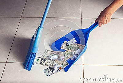 Woman broom sweeps dollars in garbage scoop on floor background Stock Photo