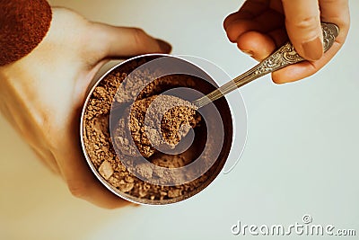 A woman in a brown jacket holds a jar of cocoa powder in her hands and takes out a portion of cocoa from it with a teaspoon. Top Stock Photo