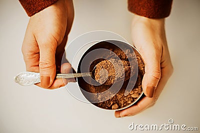 A woman in a brown jacket takes out a portion of fragrant crumbly cocoa powder from a jar with a beautiful silver teaspoon. The Stock Photo