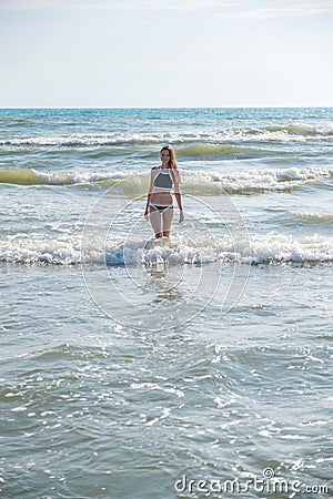 Woman bruenette with long hair in blue bikini going to swim in the wave`s sea. Front view. Stock Photo