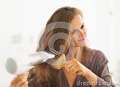 Woman brushing and blow drying hair in bathroom Stock Photo