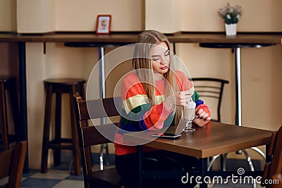 A woman in a cafe is drinking coffee, a beautiful sweater is on the girl, a beautiful young girl is waiting for her man Stock Photo