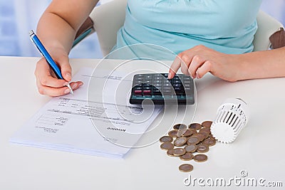 Woman calculating invoice by coins and thermostat at desk Stock Photo