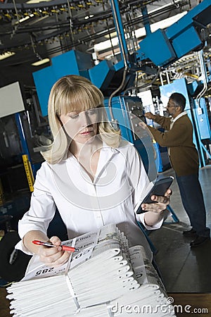 Woman With Calculator Checking Newspaper In Factory Stock Photo