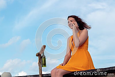 Woman seated on a pier in a tropical location using his smartphone and smiling. Sky with clouds as background Stock Photo