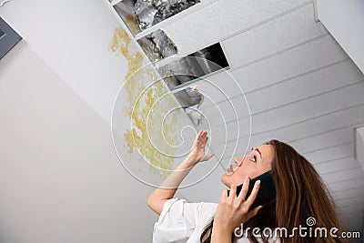 Woman Calling Plumber While Looking At Ceiling Stock Photo