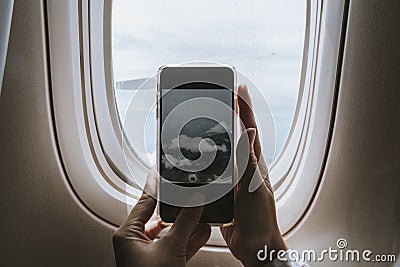 Woman capturing clouds from the plane window with her phone Stock Photo