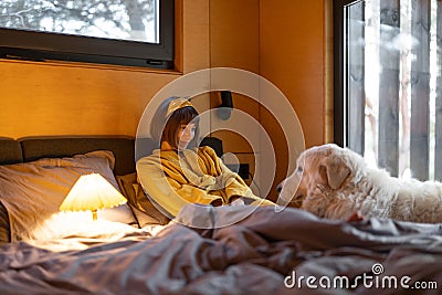Woman cares her dog while lying in bed in tiny bedroom of wooden cabin on nature Stock Photo