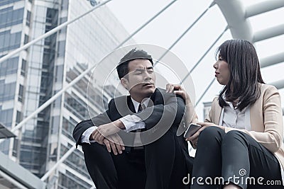 The woman caring the frustrated businessman with failed business sitting on the stairs in downtown Stock Photo
