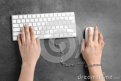 Woman chained to computer keyboard at grey table, top view. Stock Photo