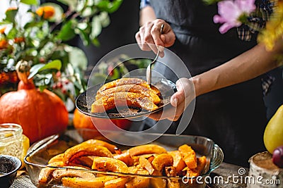 Woman chef holding slices of baked orange pumpkin with honey and cinnamon. Autumn food in a cozy kitchen. Close up Stock Photo