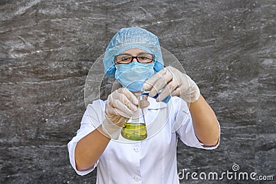 Woman chemist in protective uniform making experiment with blue and yellow flask Stock Photo