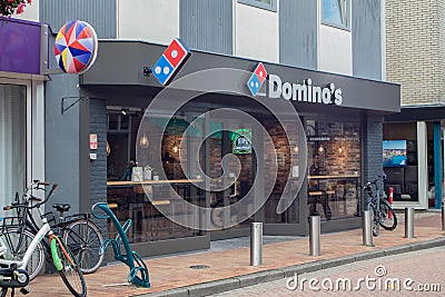 Woman with child on a bicycle riding past Domino`s pizza delivery restaurant branch Editorial Stock Photo