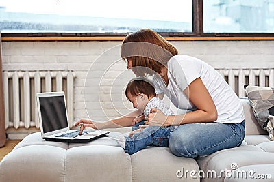 A woman with a child at a laptop sitting on a sofa. Work at home, freelancer, work during maternity leave for remote Stock Photo