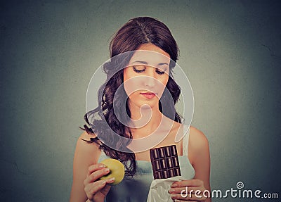 Woman with chocolate and apple trying to make a healthy choice control her body weight. Dieting concept Stock Photo