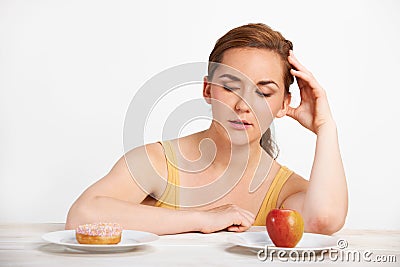 Woman Choosing Between Apple And Doughnut For Snack Stock Photo