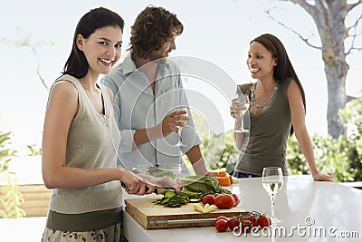 Woman Chopping Vegetables With Friends Communicating At Kitchen Counter Stock Photo