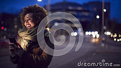 Woman On City Street At Night Ordering Taxi Using Mobile Phone App Stock Photo