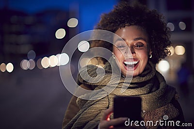 Woman On City Street At Night Ordering Taxi Using Mobile Phone App Stock Photo