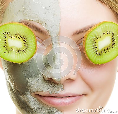 Woman in clay facial mask covering eyes with kiwi Stock Photo