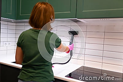 Woman cleaning tiles in the kitchen with steam machine. Stock Photo