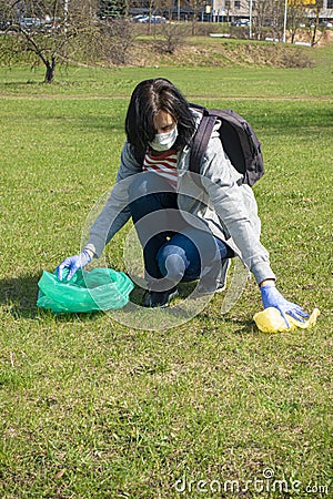 Woman cleaning up nature of garbage. Volunteer hands with blue gloves picking up trash into plastic bag. Volunteering Stock Photo