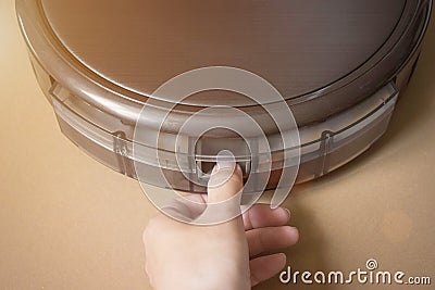 Woman cleans trash bin automatic robot vacuum cleaner. Modern smart electronic housekeeping technology. Indoor, housework Stock Photo
