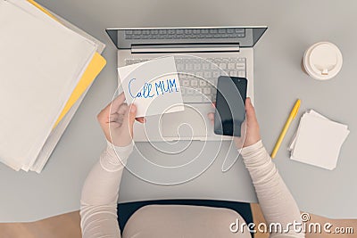 Woman clerk is sitting at office table holding note sticker with message call mum Stock Photo