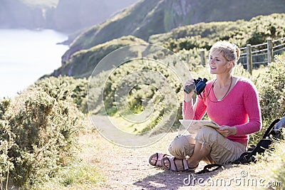 Woman on cliffside path using binoculars Stock Photo