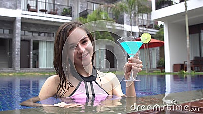 Woman clinking a glass with blue coctail to camera and drinking on luxury villa. Stock Photo