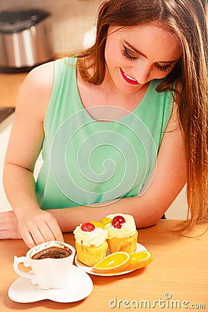 Woman with coffee and cake in kitchen. Gluttony. Stock Photo